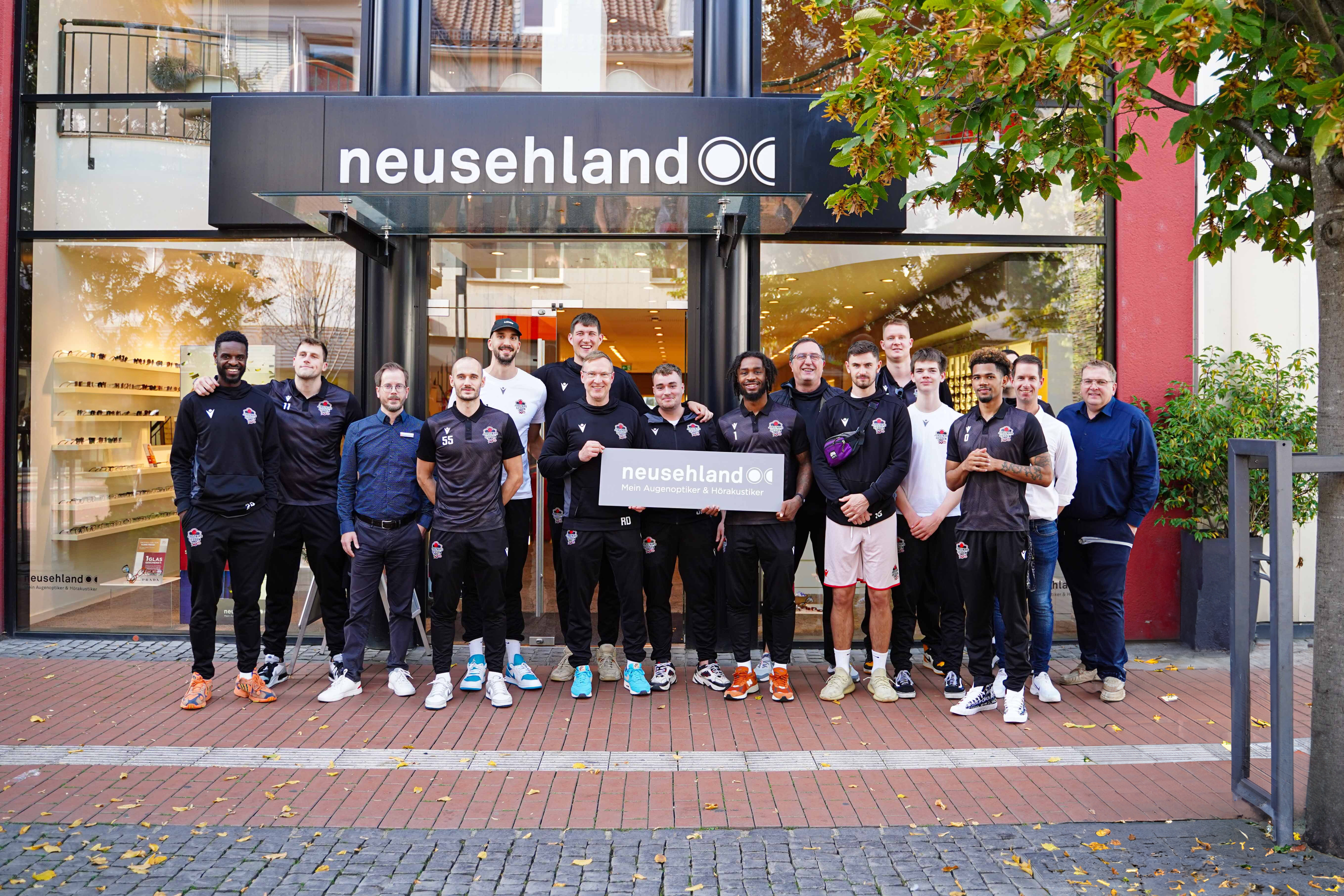 Spieler der GIESSEN 46ers stehen vor dem Neusehland Standort in Gießen und präsentieren ein Neusehland Schild