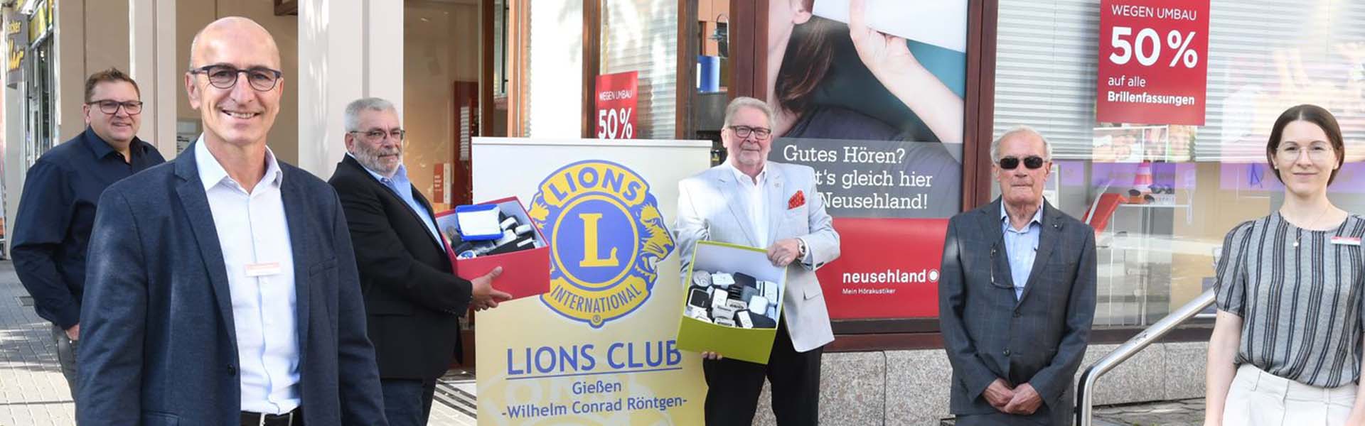 Mann mit Karton voller Hörgeräte vor einem Lions-Club-Schild