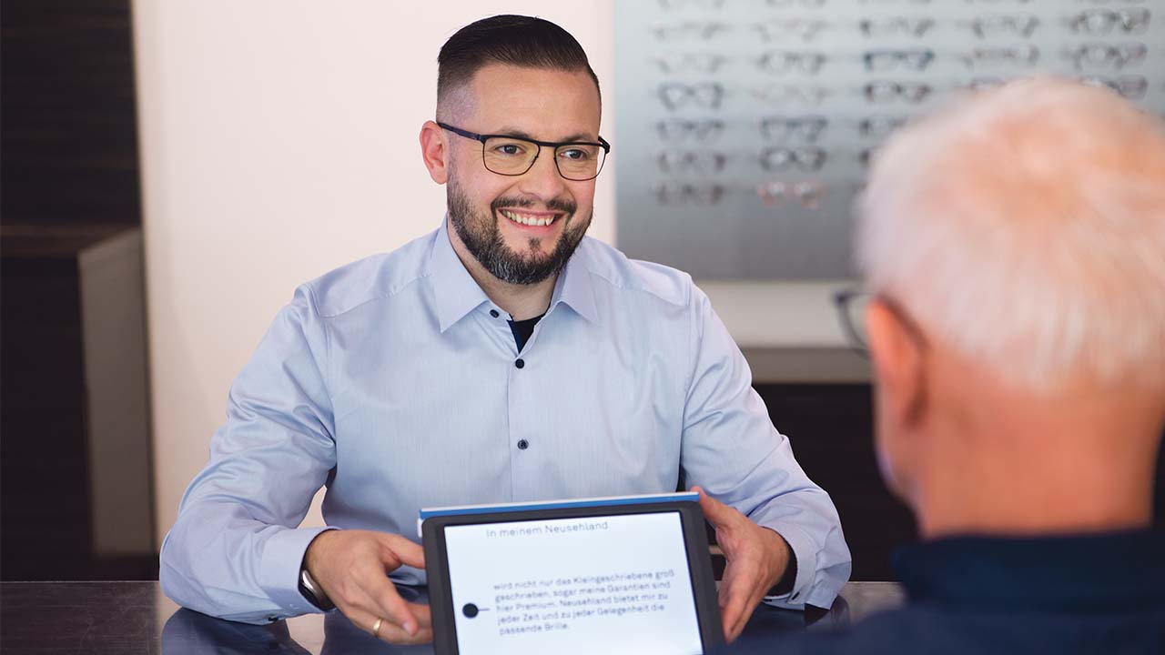 Mann mit Brille demonstriert eine elektronische Sehhilfe in einer Beratungssituation