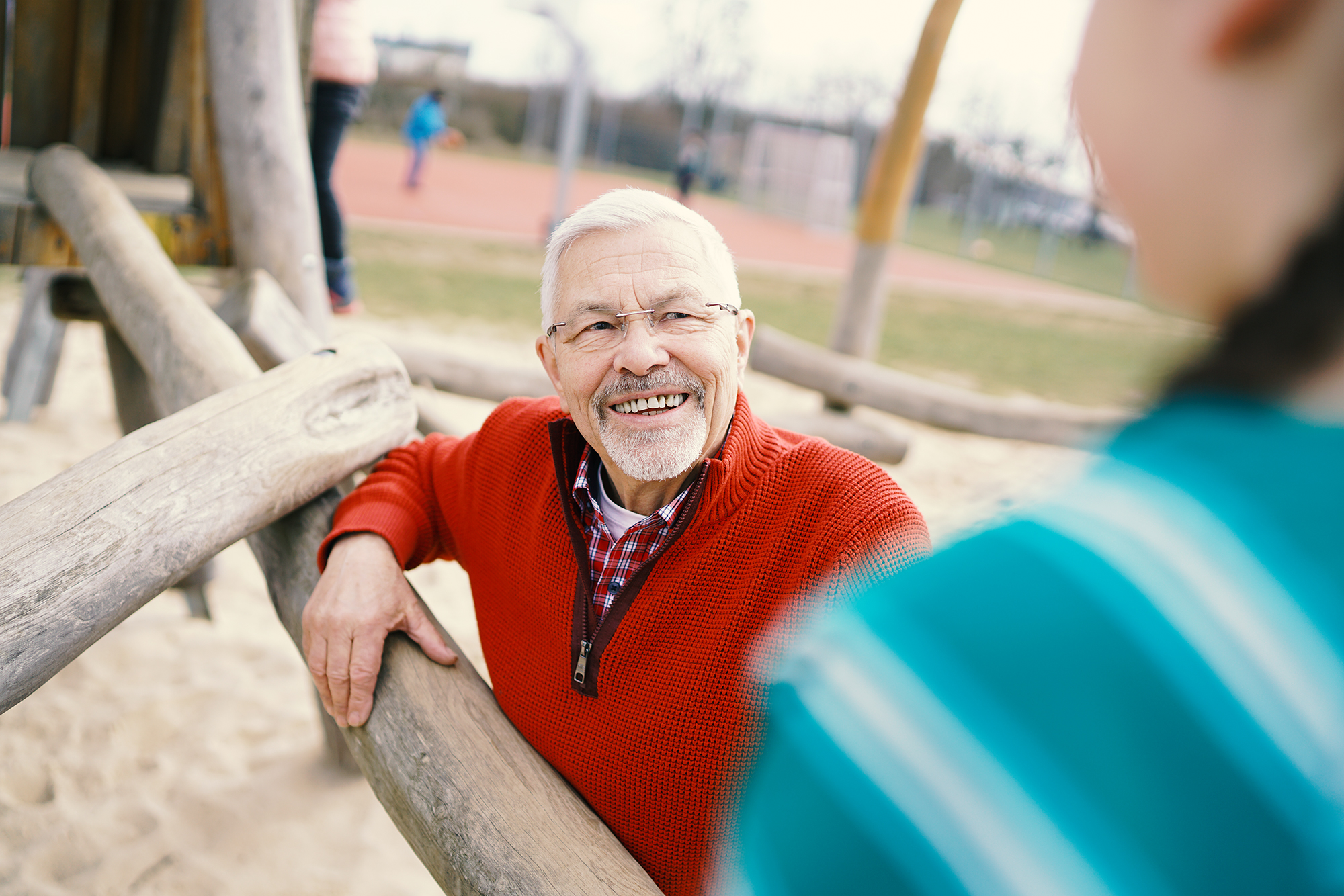 Älterer Mann unterhält sich lächelnd auf einem Spielplatz mit einer anderen Person