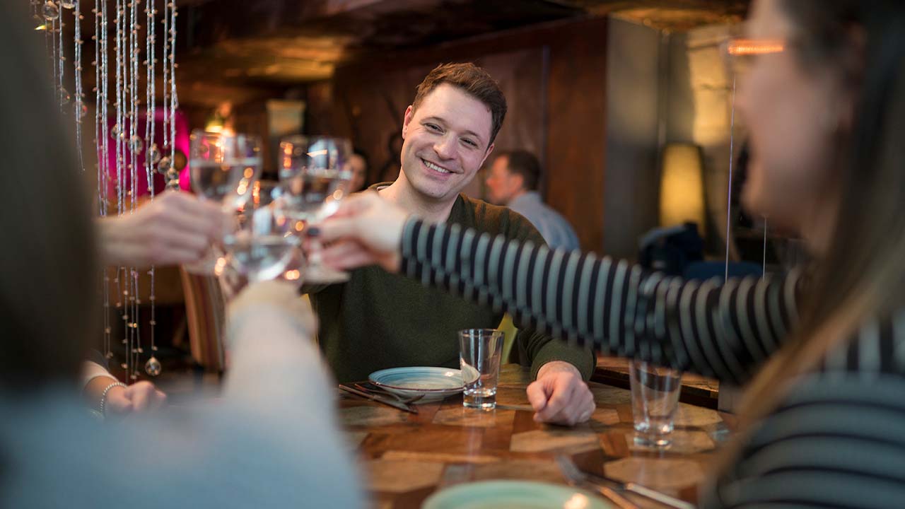Mehrere Personen sitzen an einem Tisch und stoßen bei einem Essen miteinander an