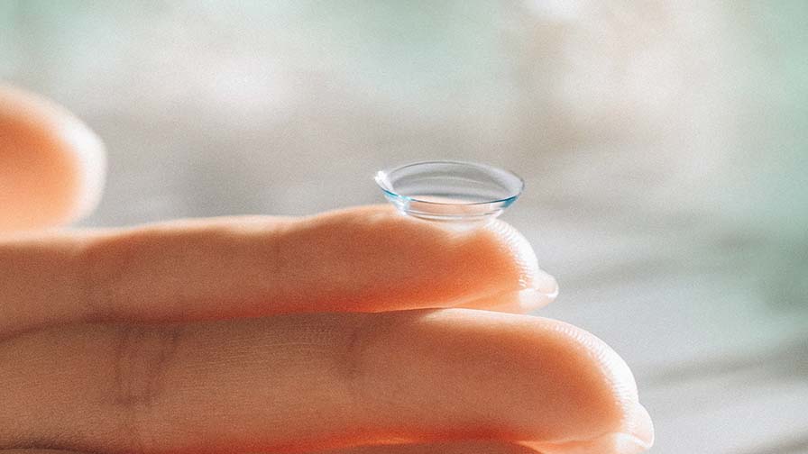 Eine Nahaufnahme einer weichen, transparenten Kontaktlinse, die auf der Fingerspitze einer Person balanciert.