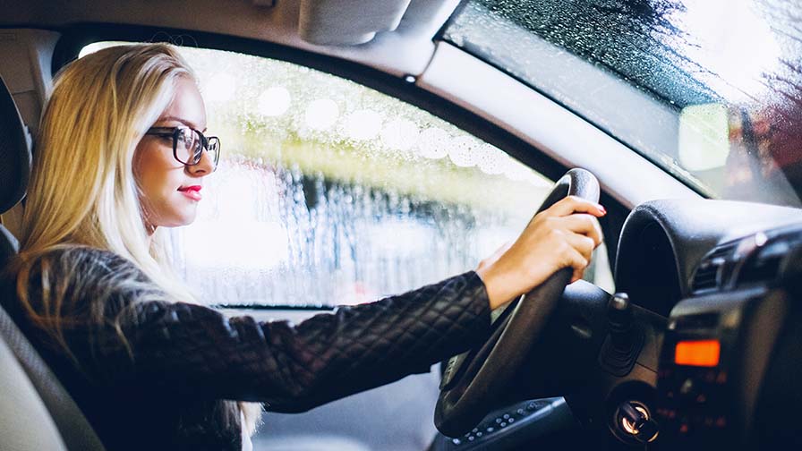 Seitliche Ansicht einer Frau, die am Steuer eines Autos sitzt und eine schwarze Brille trägt.