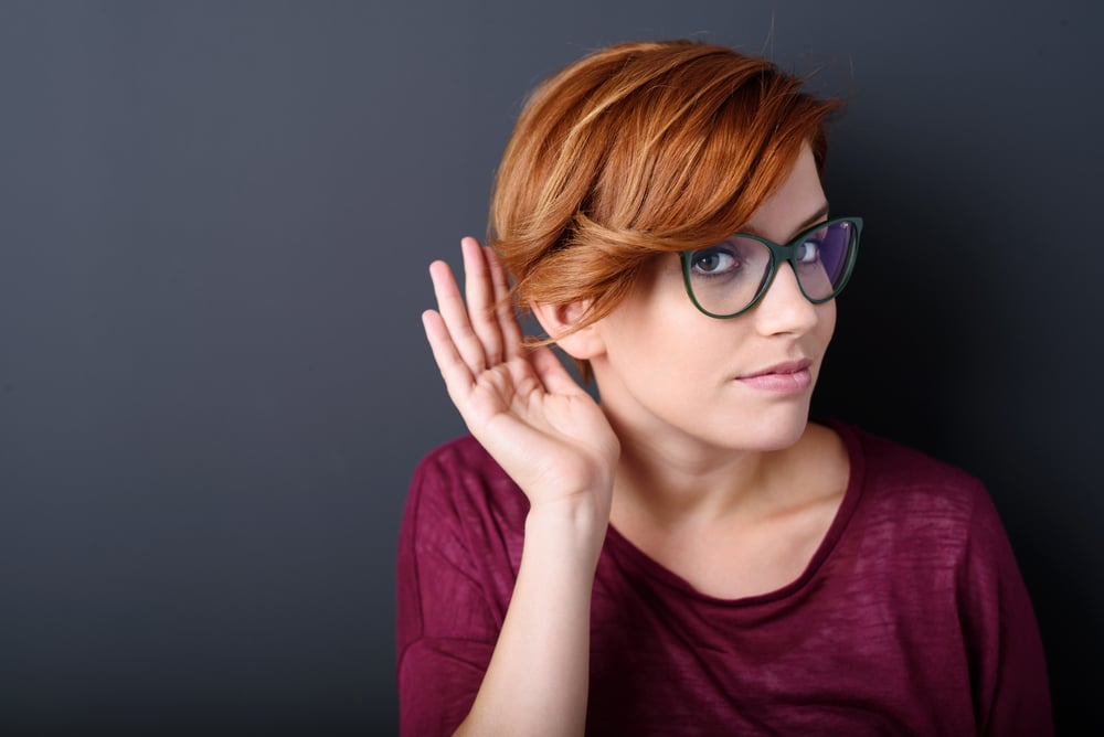 Rothaarige Frau mit Brille hört aufmerksam zu und hält die Hand ans Ohr